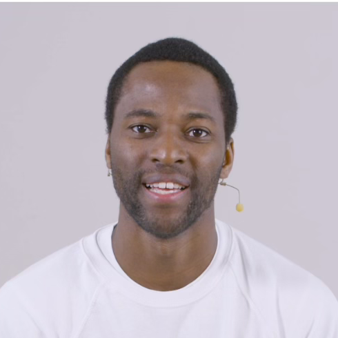 A Black man with short hair and facial stubble, wearing a white fitness t-shirt with the Living in Fitness logo, photographed against a plain white background.