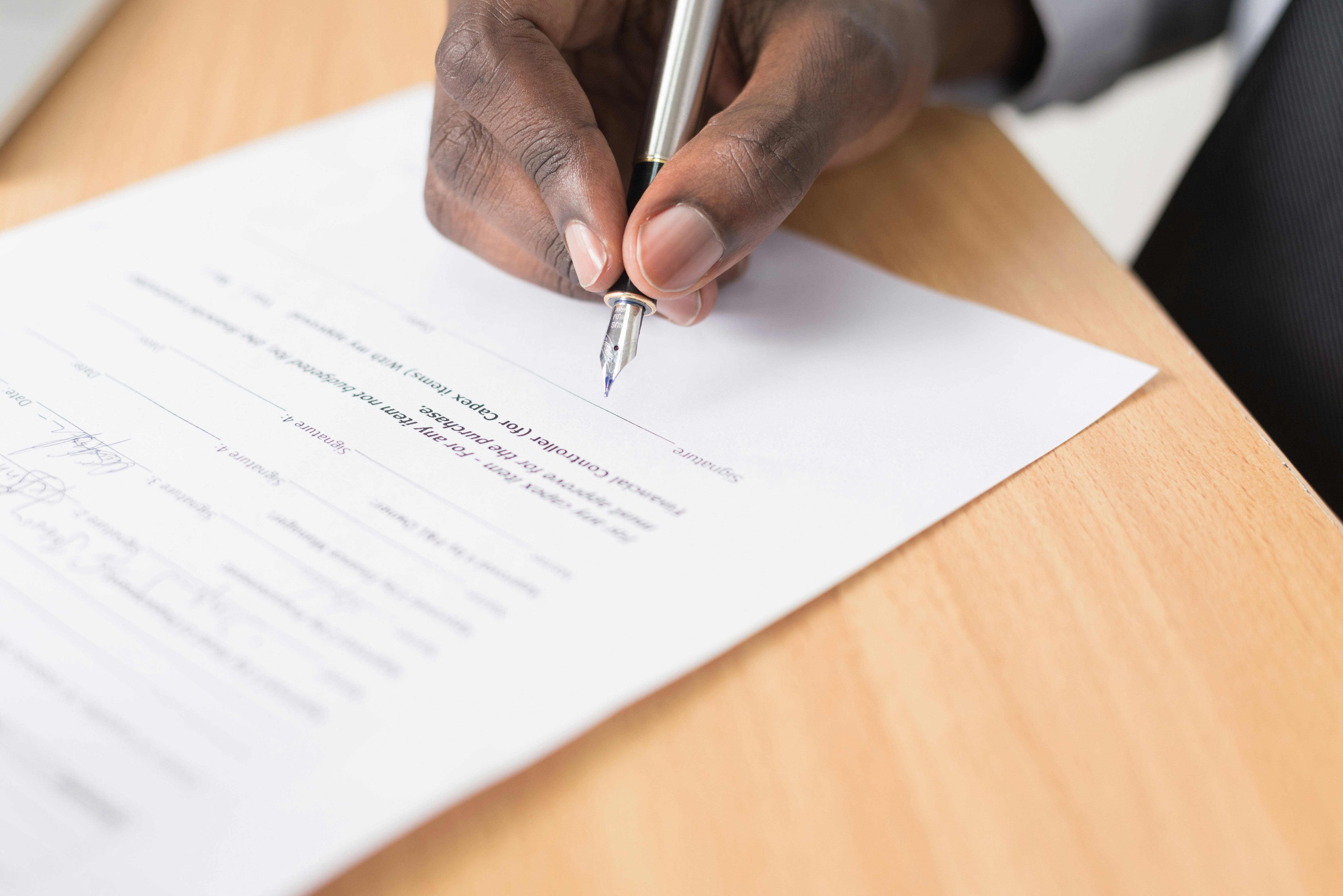 The hands of a black man holding a silver pen writing on a legal document